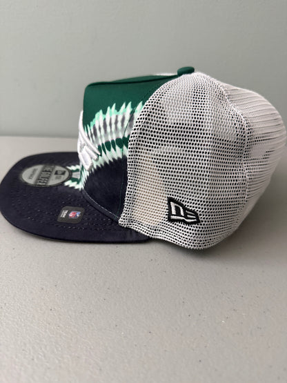 Side View: Front profile shot of a brand new New Era New York Jets The Golfer snapback hat featuring a green and white sublimated tie dye front panel, premium embroidered white jets logo, gray structured brim, and breathable white mesh trucker backing. 