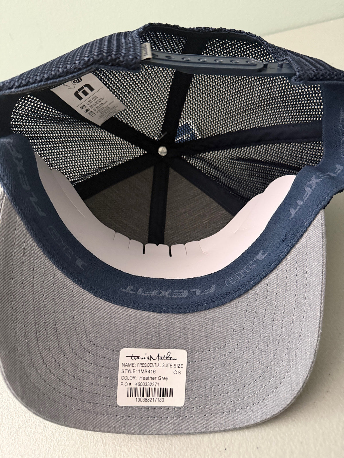 Inside View: Brand new Travis Mathew Bush Wood CC 1980 Caddy Day Golf Tournament Champion trucker hat featuring a heather gray structured crown, an embroidered champion patch, dark blue mesh backing, and a gold FlexFit 110 sticker from Bell's Bargain Barn.