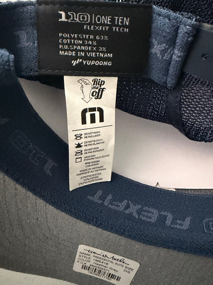 Brand Tag:  Brand new Travis Mathew Bush Wood CC 1980 Caddy Day Golf Tournament Champion trucker hat featuring a heather gray structured crown, an embroidered champion patch, dark blue mesh backing, and a gold FlexFit 110 sticker from Bell's Bargain Barn.