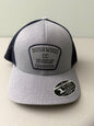Brand new Travis Mathew Bush Wood CC 1980 Caddy Day Golf Tournament Champion trucker hat featuring a heather gray structured crown, an embroidered champion patch, dark blue mesh backing, and a gold FlexFit 110 sticker from Bell's Bargain Barn.