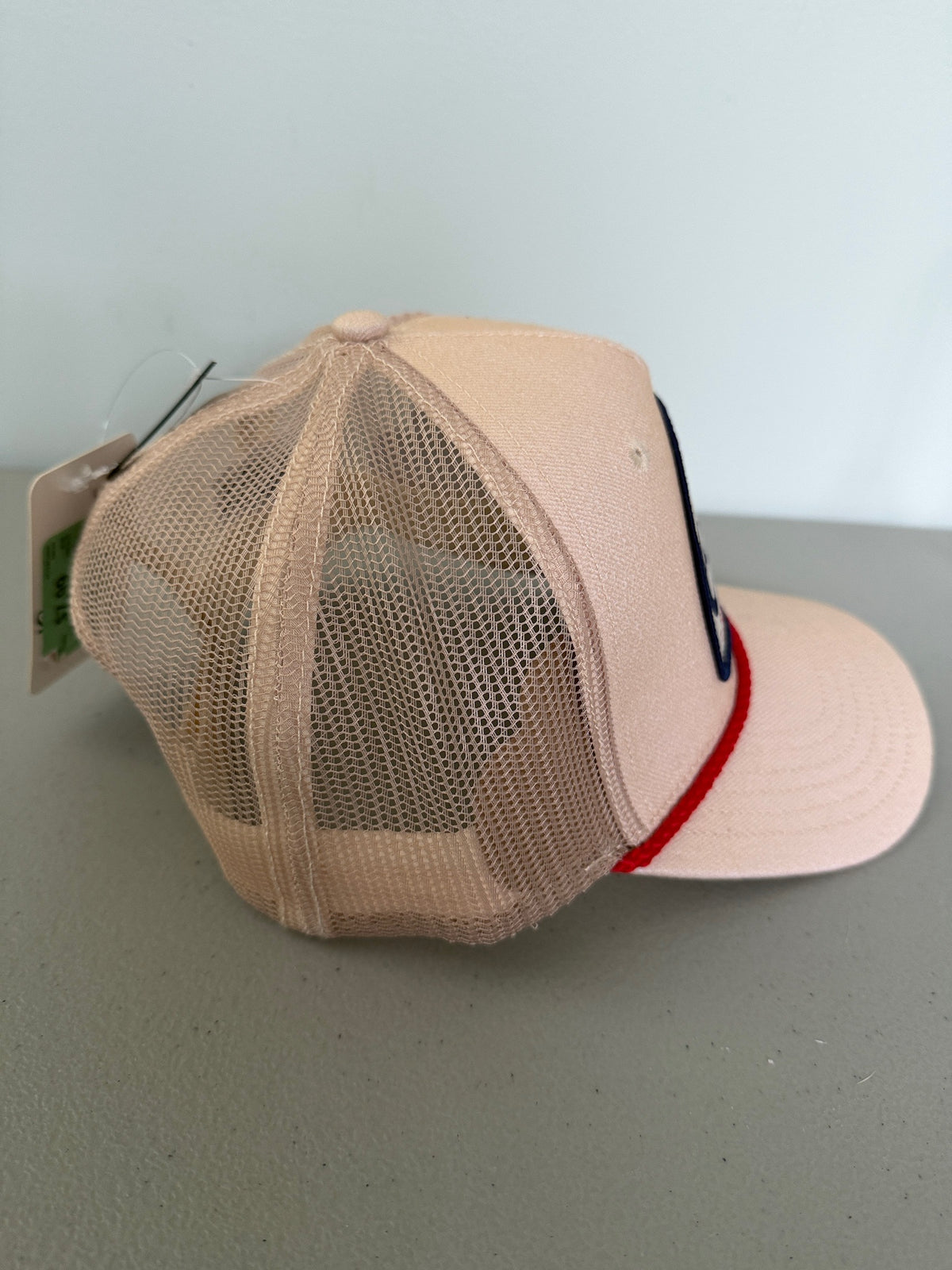 Side View: Brand new Coors Banquet Beer Fy Fishing mesh trucker hat featuring a cream structured crown, an embroidered oval patch with a rainbow trout graphic, tan mesh panels, a bright red braided front visor rope, and a snapback closure from Bell's Bargain Barn