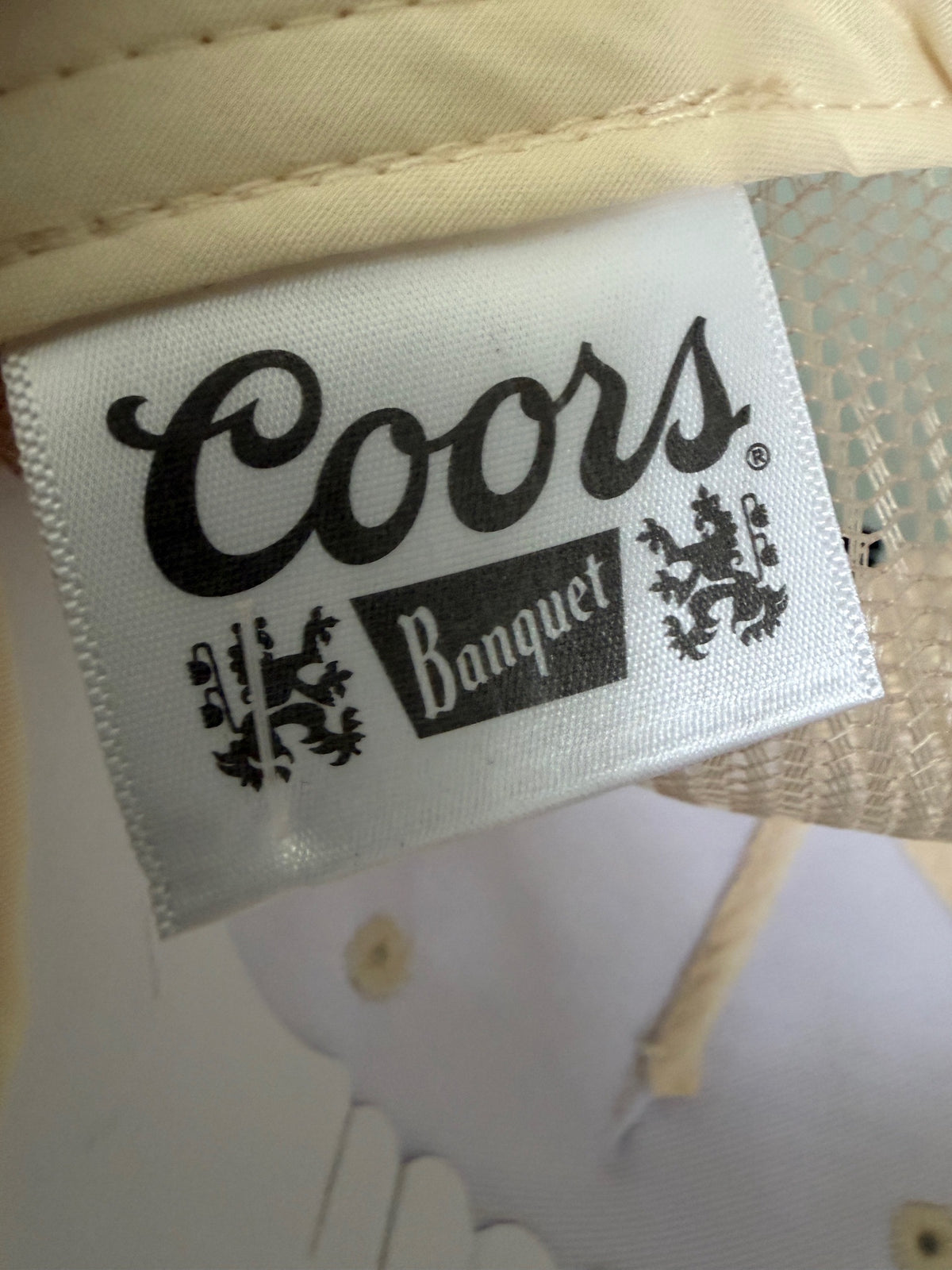 Brand Tag View: Brand new Coors Banquet Beer Fy Fishing mesh trucker hat featuring a cream structured crown, an embroidered oval patch with a rainbow trout graphic, tan mesh panels, a bright red braided front visor rope, and a snapback closure from Bell's Bargain Barn