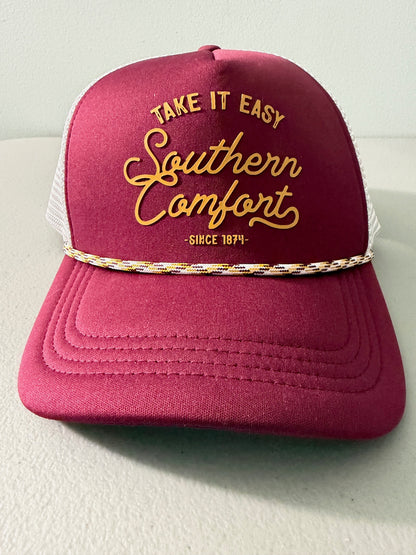 Brand new Southern Comfort Take It Easy mesh trucker hat featuring a structured maroon front foam panel, raised gold cursive lettering, white mesh back panels, a patterned front visor accent rope, and an adjustable snapback closre from Bell's Bargain Barn. 