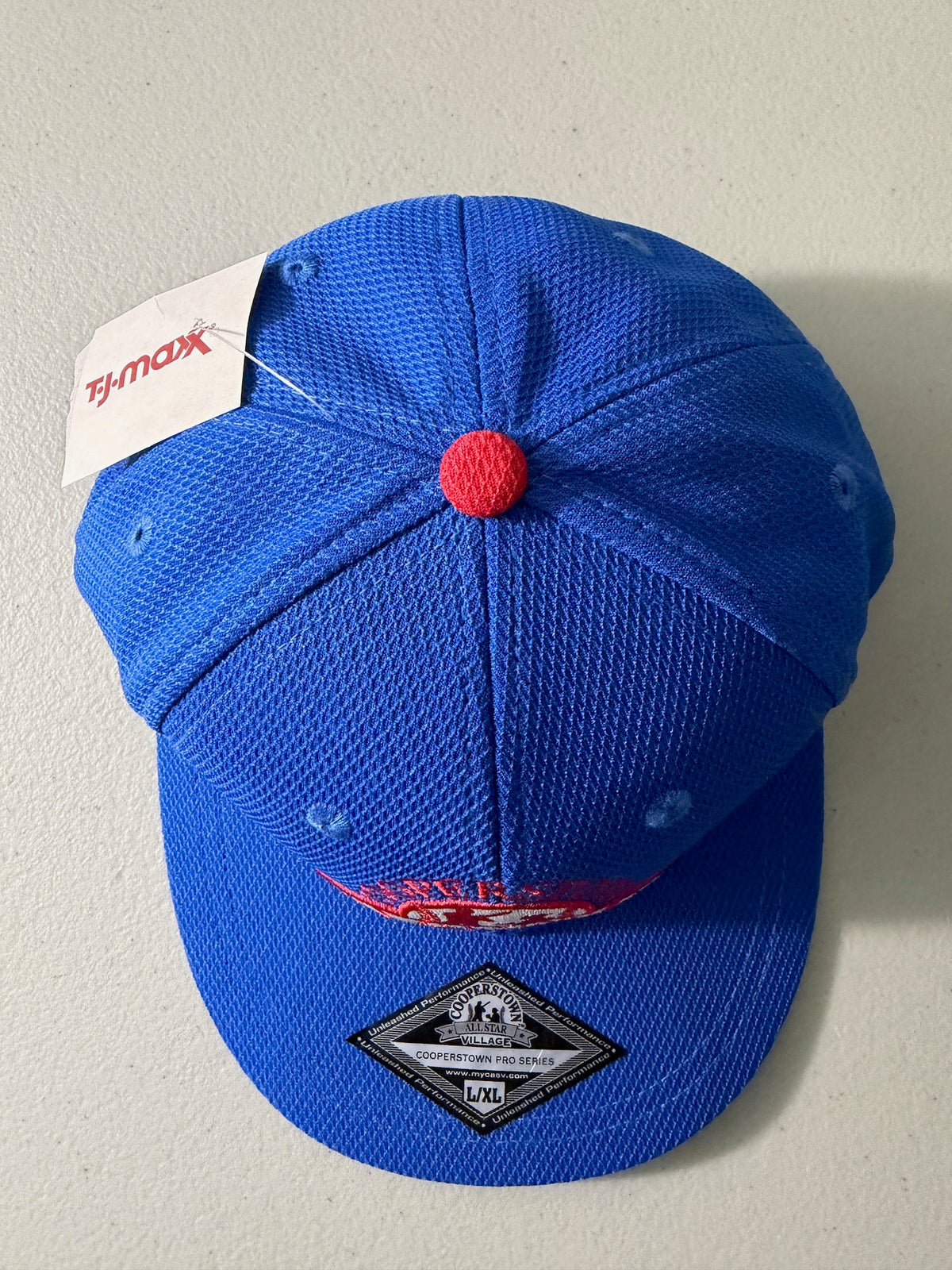 Top View: Brand new royal blue Cooperstown All Star Pro Village Pro Series stretch fit baseball hat featuring an embroidered red and white tournament patch, a diamond-shaped L/XL silver visor sticker, and an athletic mesh-textured crown from Bell's Bargain Barn. 