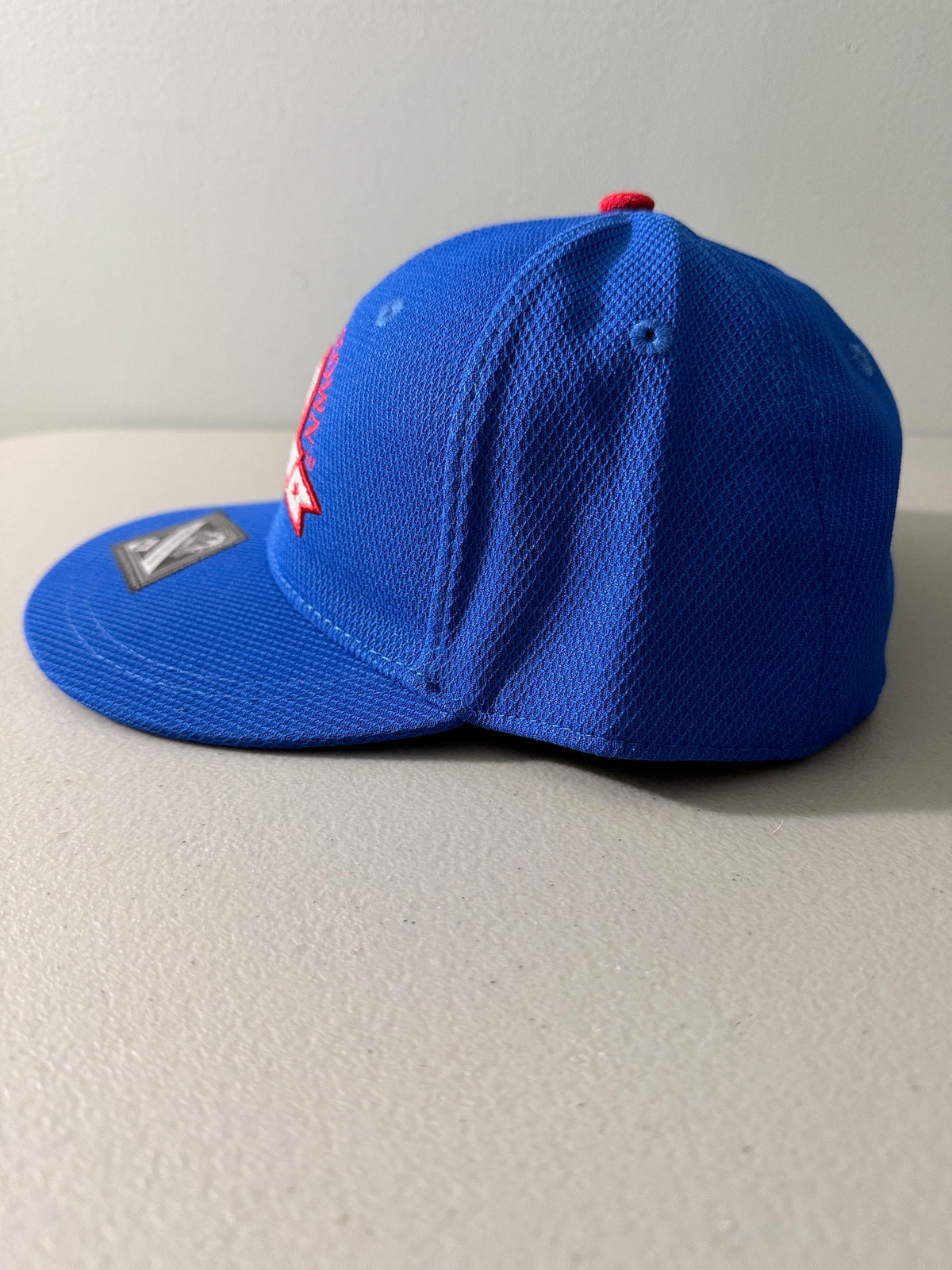 Side View: Brand new royal blue Cooperstown All Star Pro Village Pro Series stretch fit baseball hat featuring an embroidered red and white tournament patch, a diamond-shaped L/XL silver visor sticker, and an athletic mesh-textured crown from Bell's Bargain Barn. 