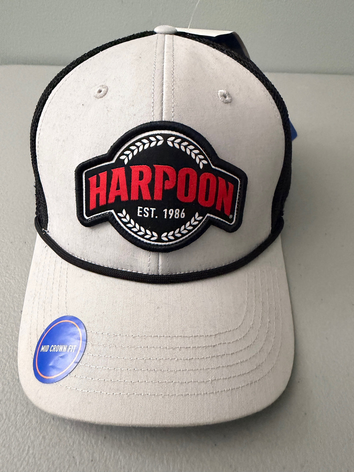 Brand new Harpoon Brewery Est. 198 mid crown fit trucker hat featuring a structured off-white front panel with a black embroidered logo patch, black mesh backing, a thin black visor rope, and a blue brim sticker from bell's Bargain Barn.