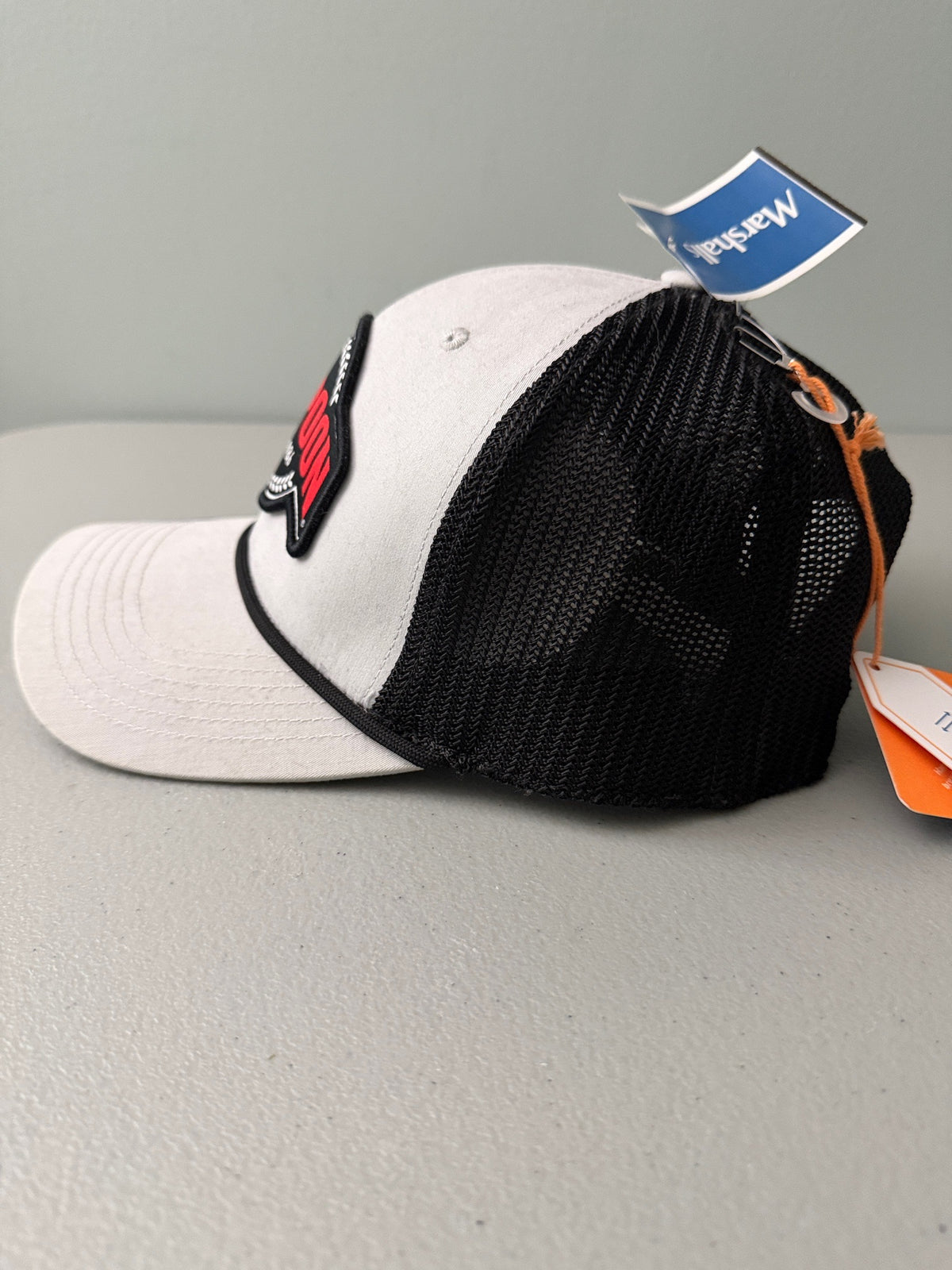 Side View: Brand new Harpoon Brewery Est. 198 mid crown fit trucker hat featuring a structured off-white front panel with a black embroidered logo patch, black mesh backing, a thin black visor rope, and a blue brim sticker from bell's Bargain Barn.