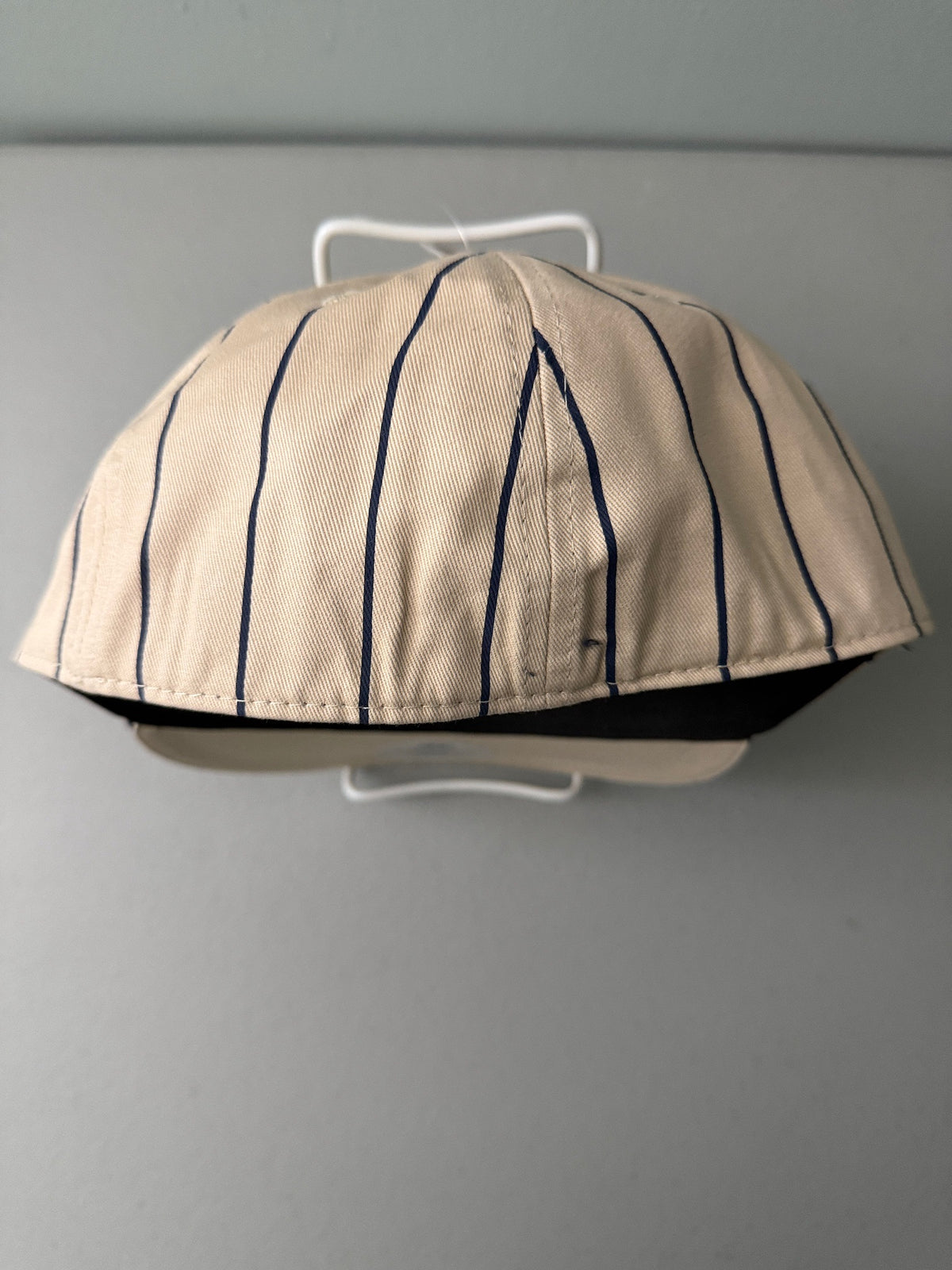 Back View: Brand new cream Cooperstown All Star Village Pro Series stretch fit baseball hat with navy blue pinstripes, featuring an embroidered navy tournament logo patch and a silver diamond-shaped L/XL visor sticker from Bell's Bargain Barn.  