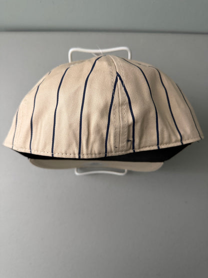 Back View: Brand new cream Cooperstown All Star Village Pro Series stretch fit baseball hat with navy blue pinstripes, featuring an embroidered navy tournament logo patch and a silver diamond-shaped L/XL visor sticker from Bell's Bargain Barn.  