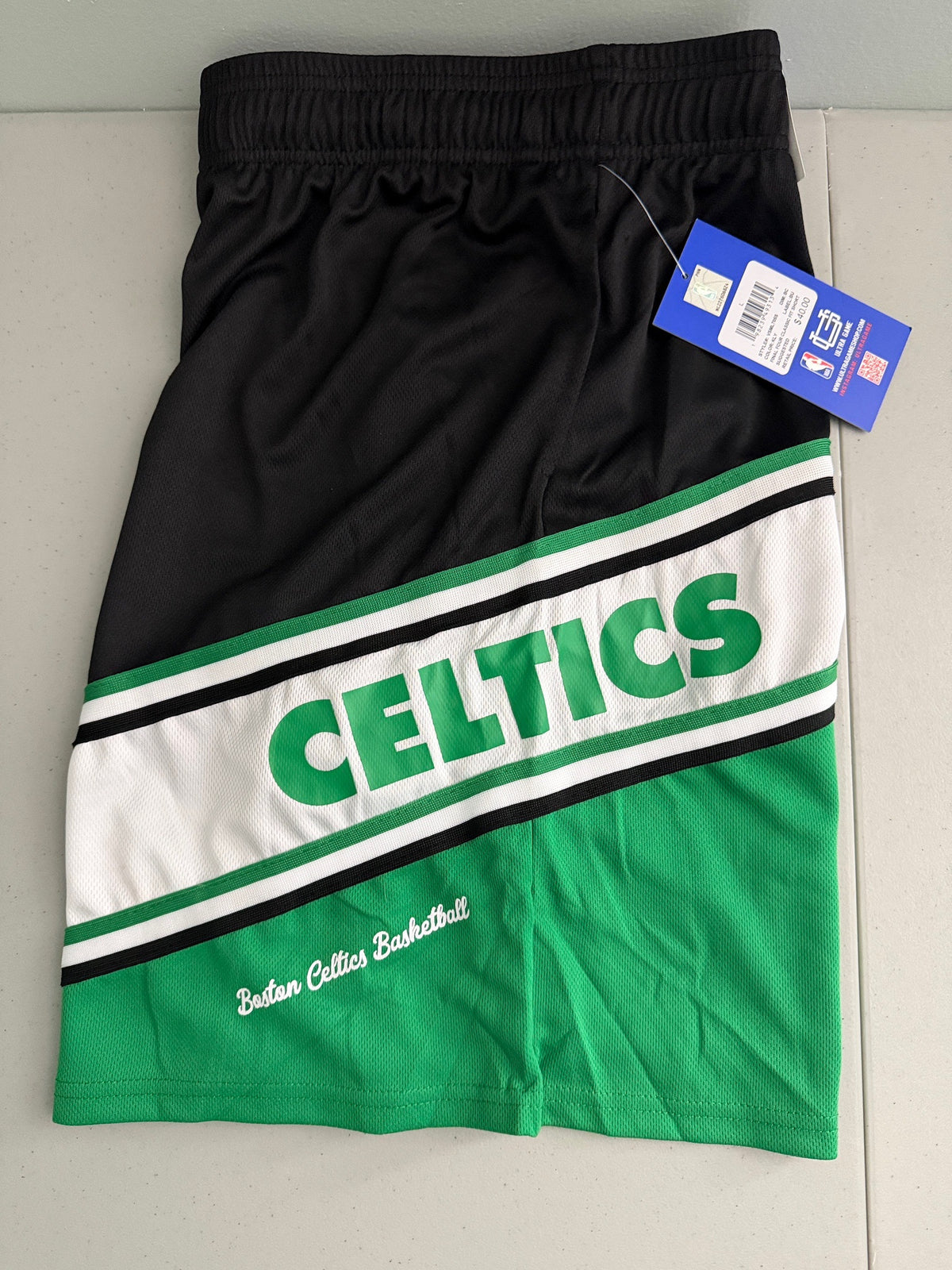 Close-up view: Boston Celtics Men's NBA basketball shorts left leg Celtics and scripted stylized Boston Celtics Basketball across the left thigh 