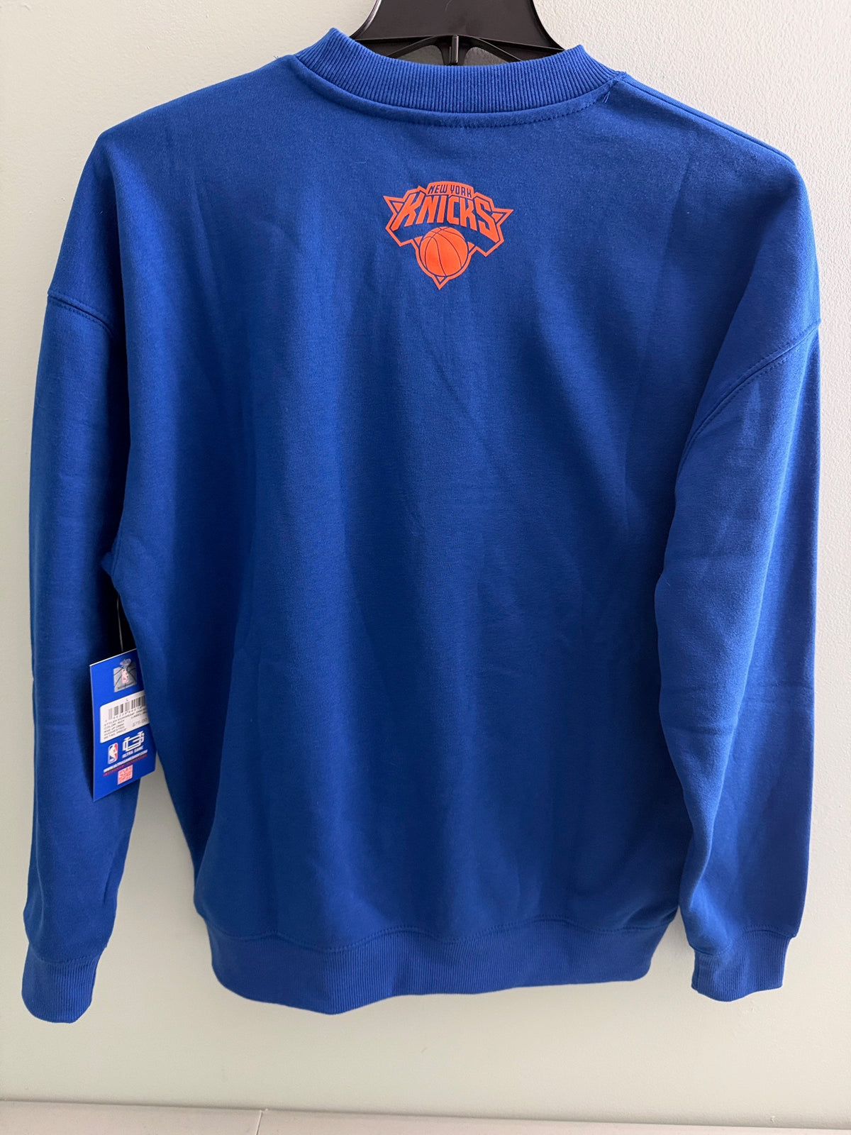 Back view of New with tags Men's New York Knicks NBA crewneck sweatshirt in royal blue featuring large orange and white graphic team logos.