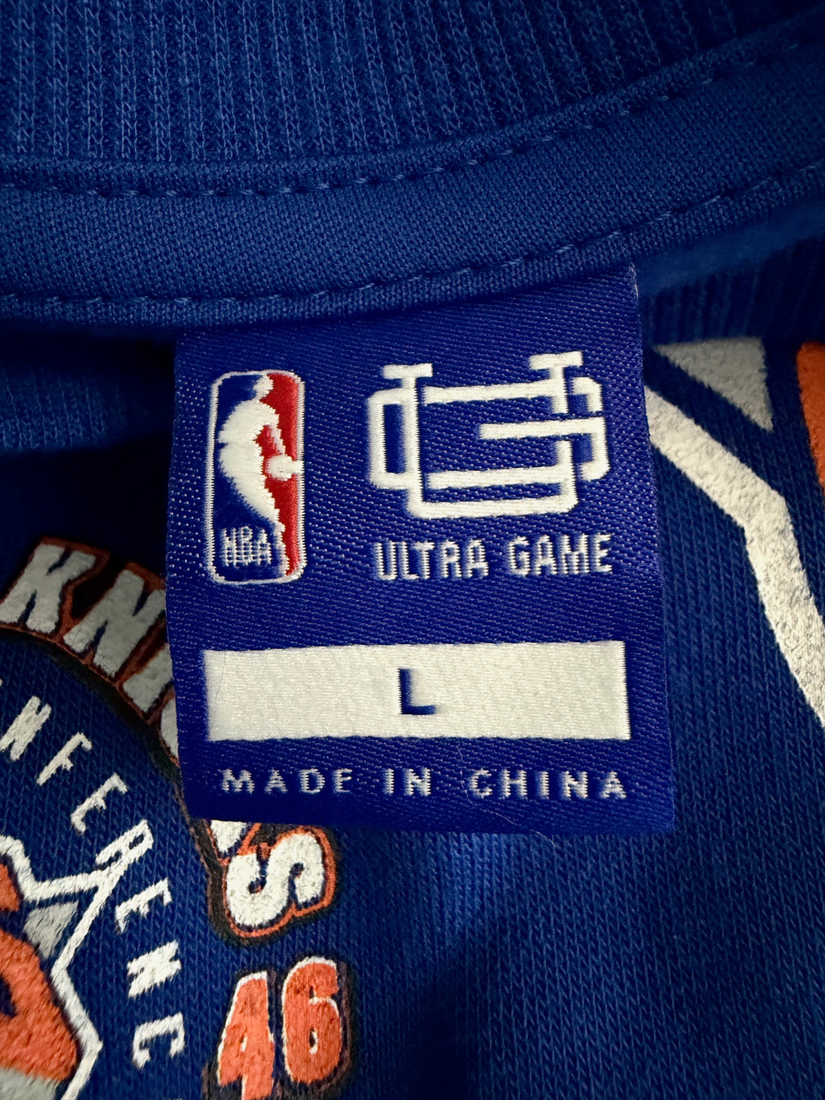 Embroidered brand Tag view of New with tags Men's New York Knicks NBA crewneck sweatshirt in royal blue featuring large orange and white graphic team logos.