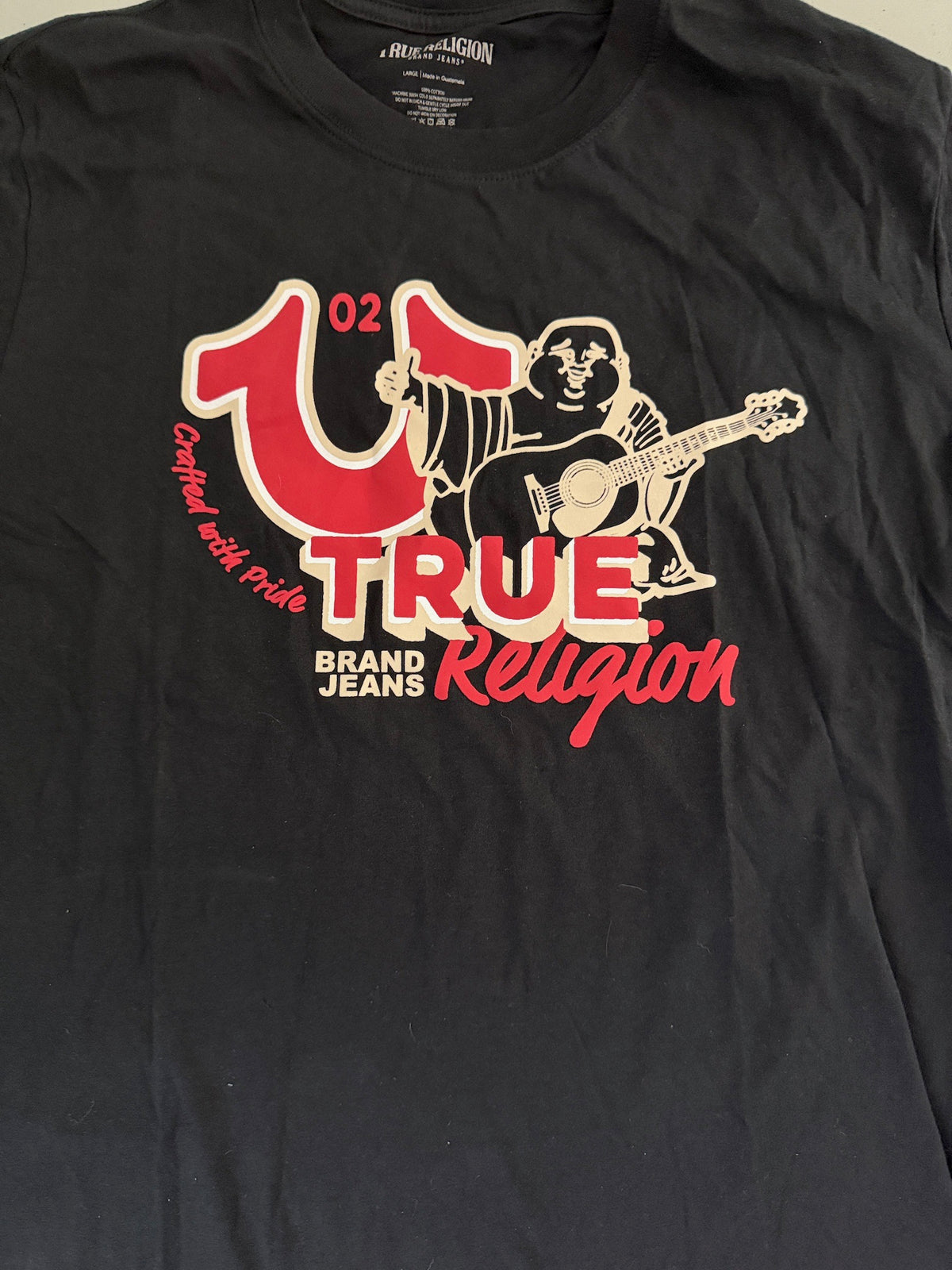 Detailed close-up of the red and white front chest graphic on the True Religion Big Horshoe Buddha T-shirt, featuring the signature oversized horseshoe and guitar-playing Buddha logo.