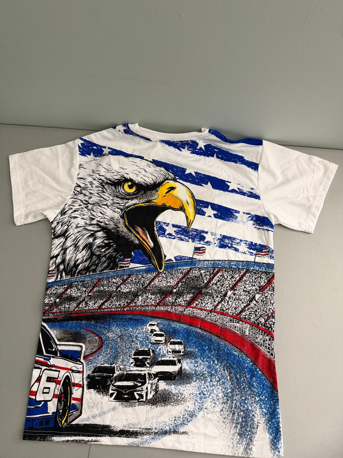Back View: The back view of the white NASCAR graphic tee shirt featuring a large illustration of an American eagle soaring over race cars on a track with packed fan grandstands