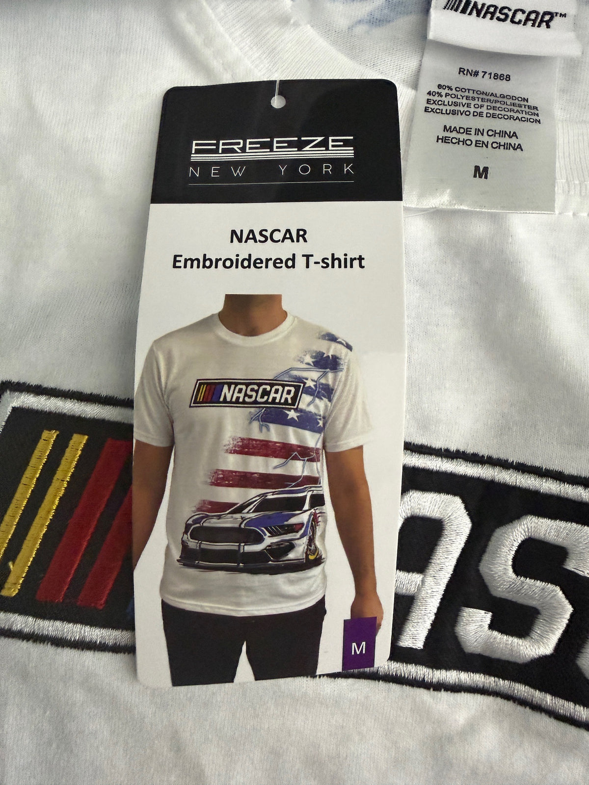 Cardboard Hang Tag: Close-up of retail cardboard hand tag attached to the white NASCAR t-shirt, clearly showing the official manufacturer logo and authentic merchandise details. 