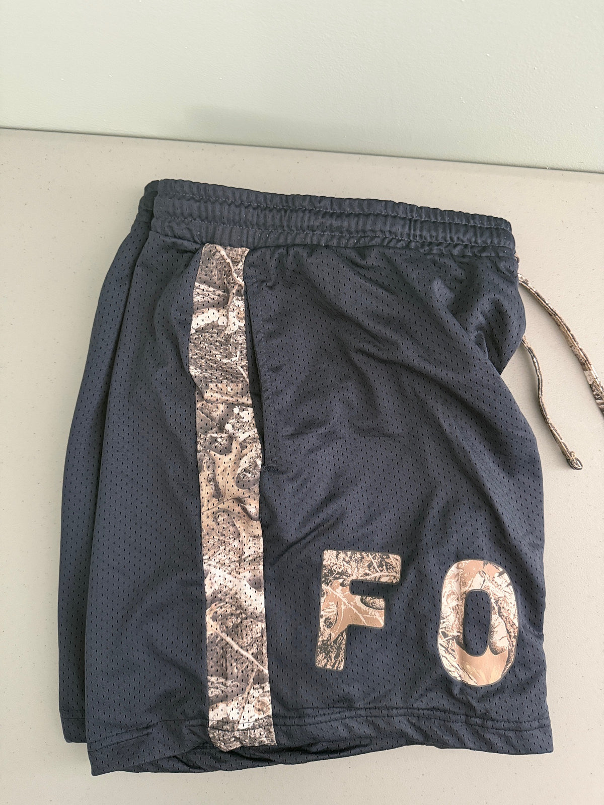 Close-up detail shot of Ford men's XXL mesh shorts highlighting the texture of the breathable navy mesh, brown camouflage pattern fabric, and deep functional side pocket. 