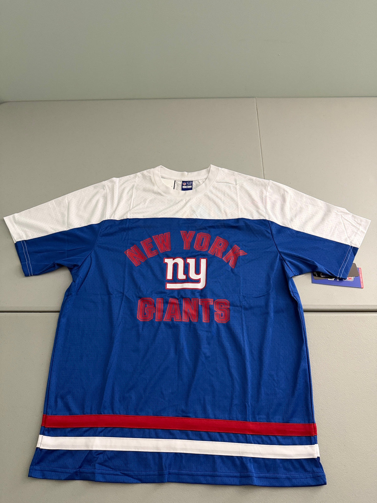 Front view of a brand new royal blue and white Ultra Game Day NFL NY Giants short-sleeve shirt. The jop features a prominent, bold screen-printed New York Giants logo across the chest, crisp white contrast blocking panels on the shoulders , and red varsity stripe details on the sleeves. 