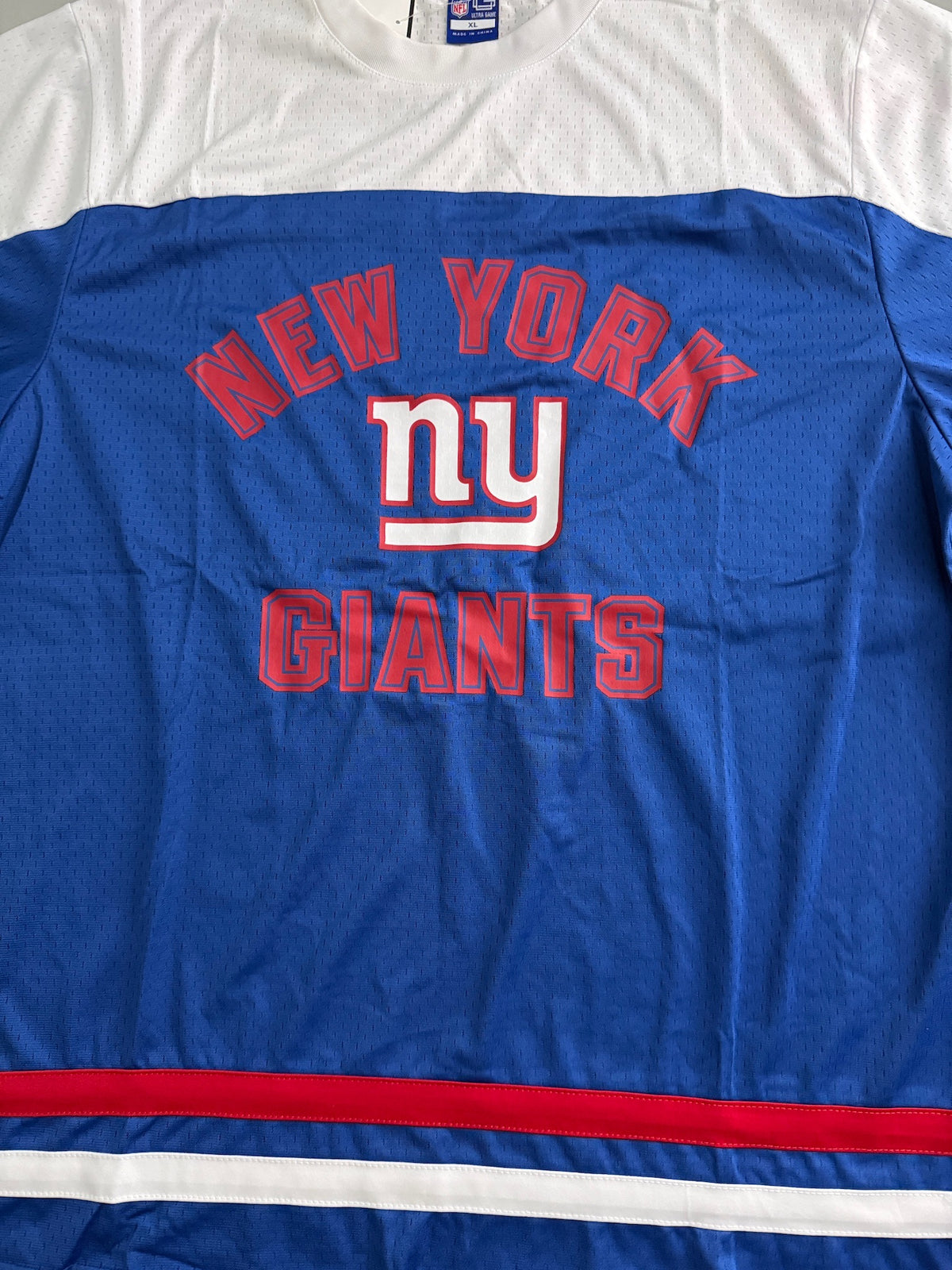Macro close-up shot focusing on the high-quality screen print of the New York Giants graphic team emblem on the front chest. The image clearly displays the fine texture of the durable 100% polyester fabric mesh weave. 