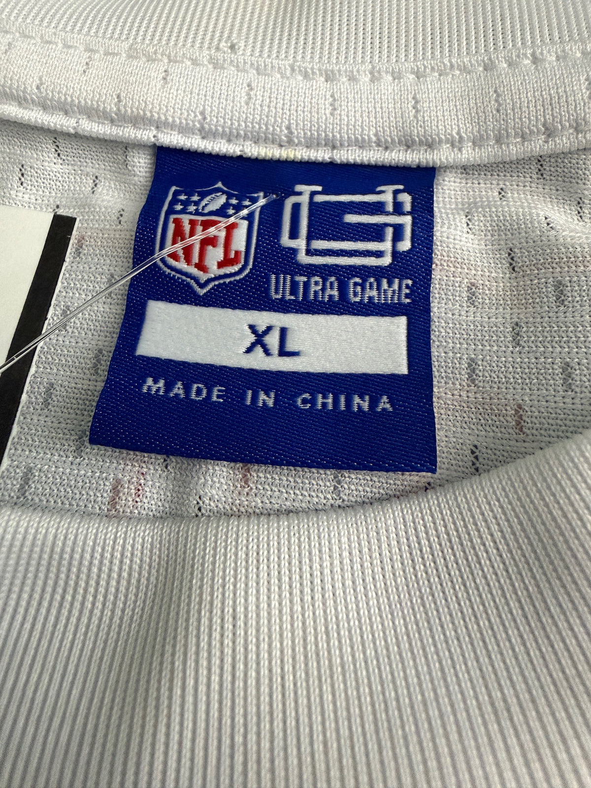 Close-up of the official attached merchandise tags on the Ultra Game shirt, showcasing the NFL logo shield, the Ultra Game Day brand name, size marking XL, and printed garment care instructions for machine washing. 