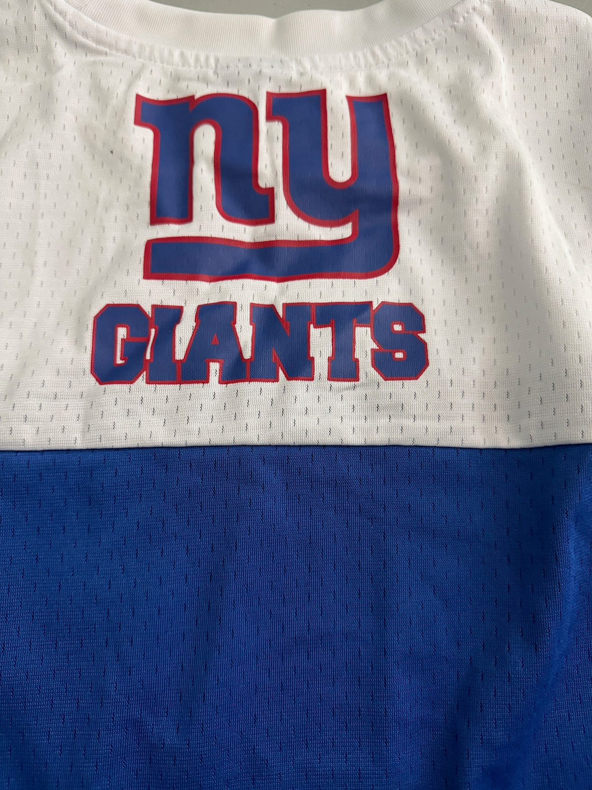 Detailed close-up shot of the secondary screen-printed New York Giants team graphic emblazoned across the back panel of the royal blue athletic shirt, highlighting the vibrant team typography and crisp color lines. 